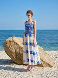 Woman wearing a pink midi dress with a tropical print and spaghetti straps on a beach with large rocks