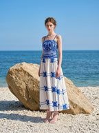 Woman wearing a pink midi dress with a tropical print and spaghetti straps on a beach with large rocks