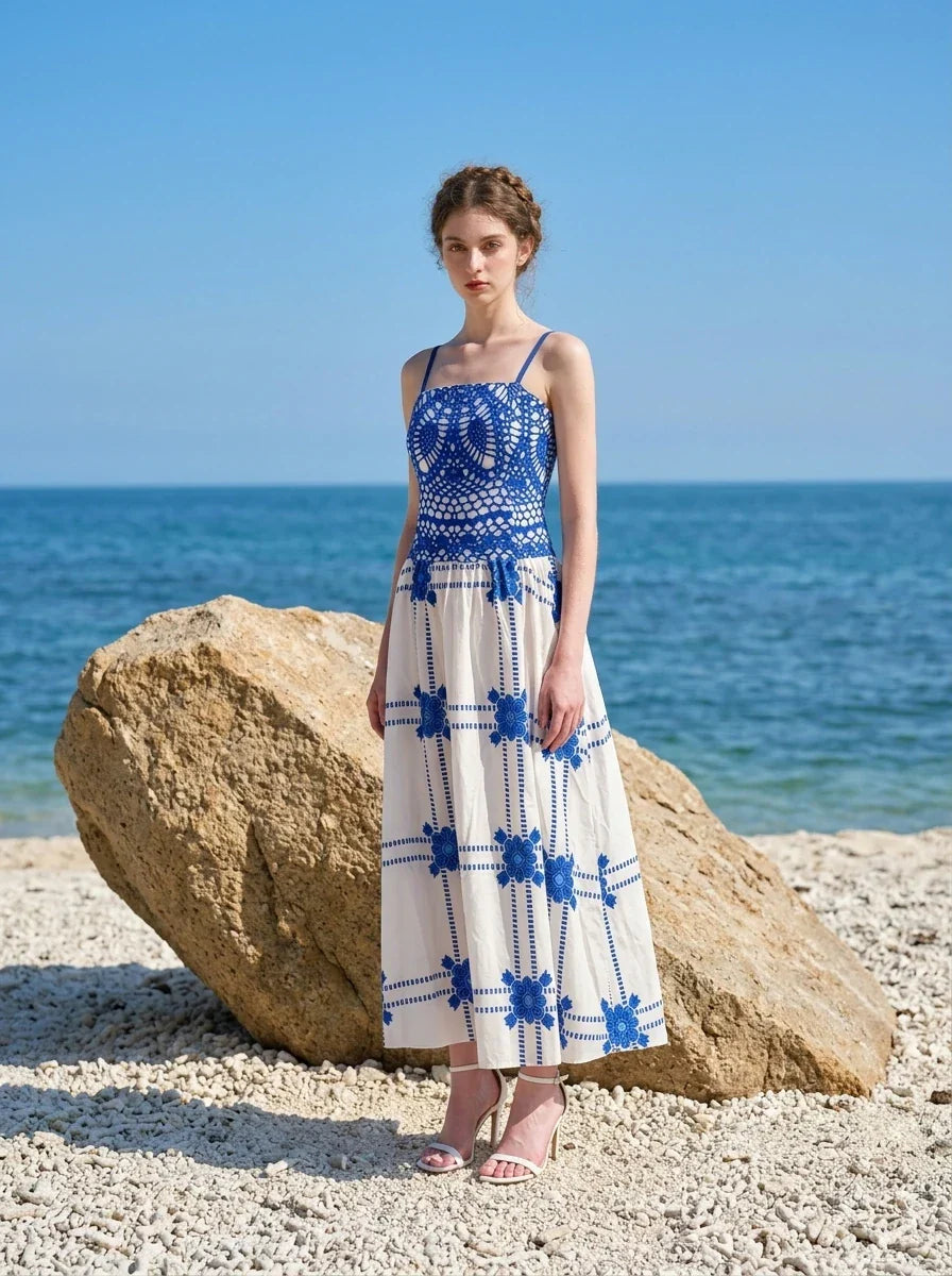 Woman wearing a pink midi dress with a tropical print and spaghetti straps on a beach with large rocks