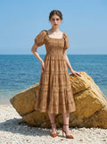 Woman posing by a large rock on a beach, wearing a tan midi dress with a smocked bodice, puff sleeves, and a print.