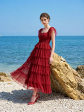 Woman posing on a rocky beach wearing a red tiered tulle dress