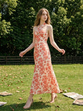 Woman walking in a field wearing a cream and coral floral print halter neck midi dress