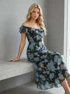 Woman sitting on a bench wearing a black floral print off-the-shoulder midi dress with blue flowers