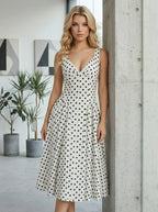 Woman standing next to a pillar in a white polka dot sleeveless dress