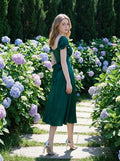 Woman in a green satin midi dress with puff sleeves and a square neckline, posing in a garden with hydrangeas.