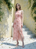 Woman in a pink floral print halter neck midi dress with ruffle trim and a high slit standing on a patio