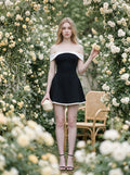Woman in a black off-the-shoulder dress with white trim standing among flowers