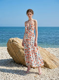 Woman posing on a beach with a large rock behind her, wearing a white floral print maxi dress.