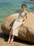 woman wearing a floral print cold shoulder midi dress sitting on a rock by the ocean