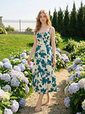 Woman in a cream and teal floral print midi dress with spaghetti straps and a tie-front bodice, walking on a garden path surrounded by hydrangeas.
