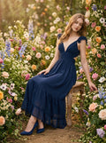 Woman sitting in a garden setting wearing a navy blue polka dot midi dress with a deep V-neck and ruffled straps.