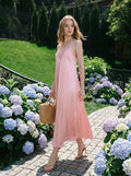 Woman walking in a garden wearing a pink satin slip dress and carrying a straw bag.