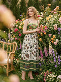 Woman wearing a white midi dress with a green smocked bodice and a colorful bird and floral print, standing in a garden with roses.