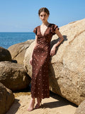 Woman in a brown polka dot midi dress with ruffled sleeves standing by rocks near the ocean.