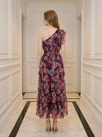 Rear view of a woman in a navy floral print one-shoulder midi dress with a tiered skirt.