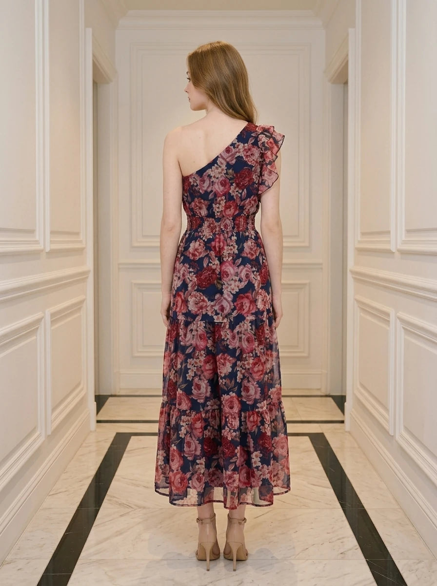 Rear view of a woman in a navy floral print one-shoulder midi dress with a tiered skirt.