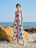 Woman posing on a beach with the ocean in the background, wearing a colorblock floral print maxi dress