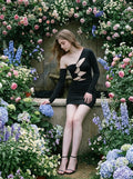 Woman in a black ruched mini dress sitting amongst flowers.