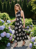 Woman in a garden wearing a black floral print halter maxi dress