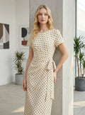 Woman leaning against a pillar wearing a cream polka dot midi wrap dress
