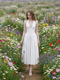 Woman walking through a field of flowers in a white halter neck midi dress.