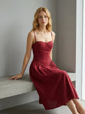 Woman sitting on a bench wearing a deep red linen blend midi dress with spaghetti straps