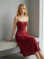 Woman sitting on a bench wearing a deep red linen blend midi dress with spaghetti straps