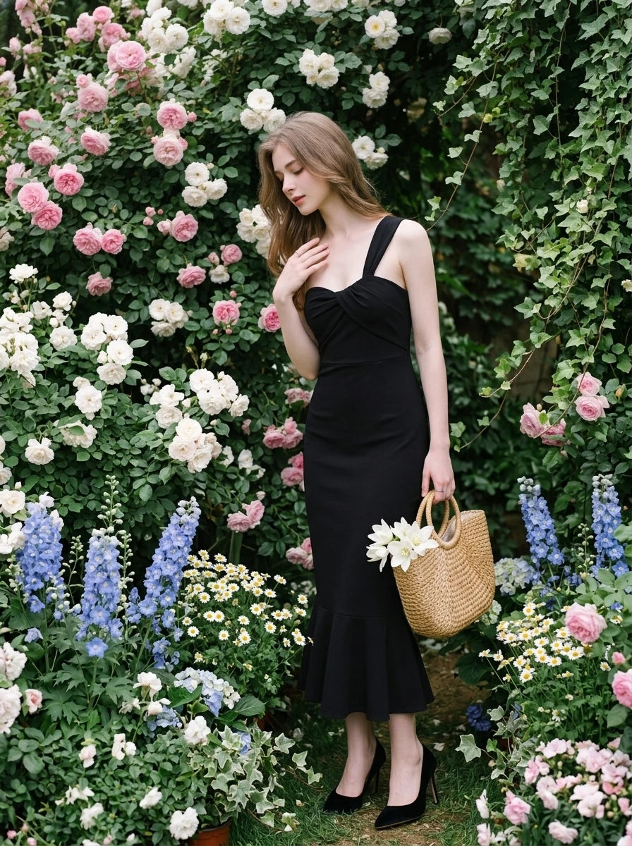 Woman in a black one-shoulder mermaid dress with a sweetheart neckline and ruched bodice, posing in a garden with roses.