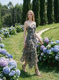 Woman walking in a garden wearing a floral print one-shoulder chiffon dress with a tiered, asymmetrical ruffle skirt.