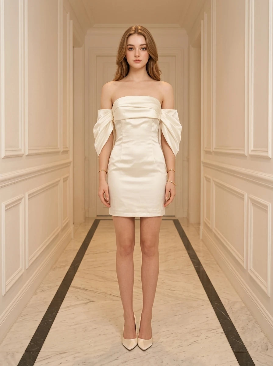 Woman in a cream off-the-shoulder satin mini dress with puff sleeves, standing in a hallway.