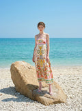 Woman in a flowing, printed sundress posing on a large rock by the sea.