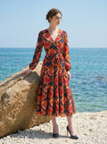 Full-length shot of a woman on a rocky shore wearing a navy blue long-sleeved floral print midi dress with a tiered skirt and wrap front.
