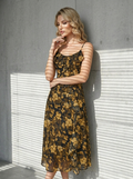 Woman posing in a floral print chiffon midi dress with ruffles against a concrete wall.