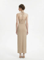 Back view of a champagne sparkly knit halter neck maxi dress with a cutout waist and thigh-high slit