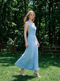 Woman walking in a light blue maxi halter dress in a grassy outdoor setting.
