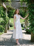 Model posing in a white halter neck midi dress in an outdoor garden setting.