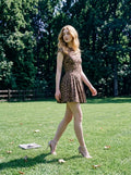 Woman in leopard print fit and flare dress walking in a grassy park.