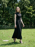 Woman wearing a sleeveless black A-line midi dress standing in a grassy field with trees.