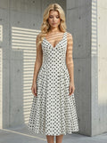 Woman posing in a white polka dot midi dress against a concrete wall with shadows