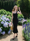 Woman in a black one-shoulder mermaid dress with a sweetheart neckline and ruched bodice, walking in a garden with hydrangeas.