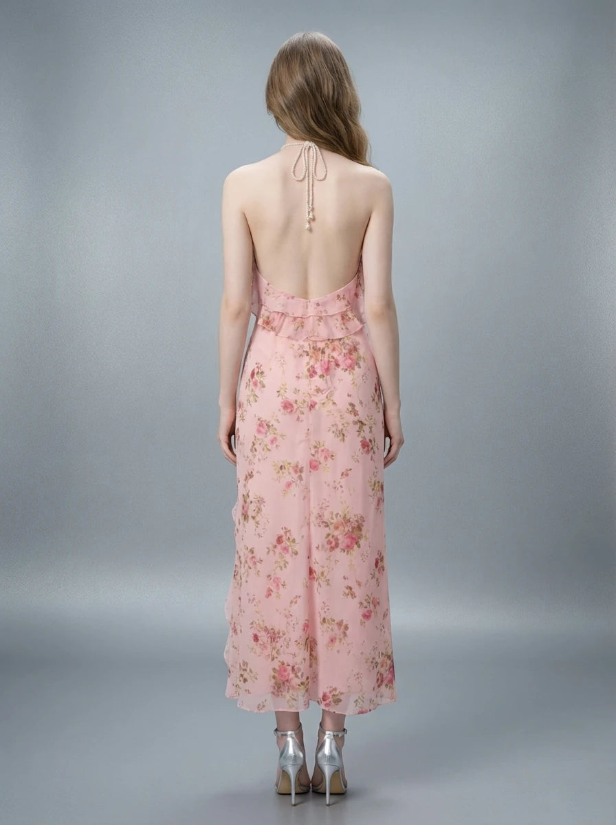 Back view of a woman in a pink floral print halter neck midi dress with an open back