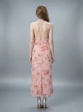 Back view of a woman in a pink floral print halter neck midi dress with an open back