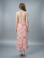 Back view of a woman in a pink floral print halter neck midi dress with an open back