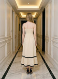 Rear view of a woman in a cream-colored midi dress with black trim and a smocked back.