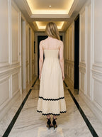 Rear view of a woman in a cream-colored midi dress with black trim and a smocked back.