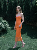 Woman walking in a garden wearing an orange slip dress with pink lace trim.