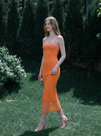 Woman walking in a garden wearing an orange slip dress with pink lace trim.