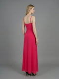 Rear view of a woman in a bright pink ruched maxi dress with spaghetti straps and butterfly details, standing against a grey backdrop.