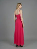 Rear view of a woman in a bright pink ruched maxi dress with spaghetti straps and butterfly details, standing against a grey backdrop.