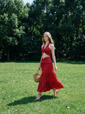 Woman in a red halter neck crop top and tiered maxi skirt walking in a park.